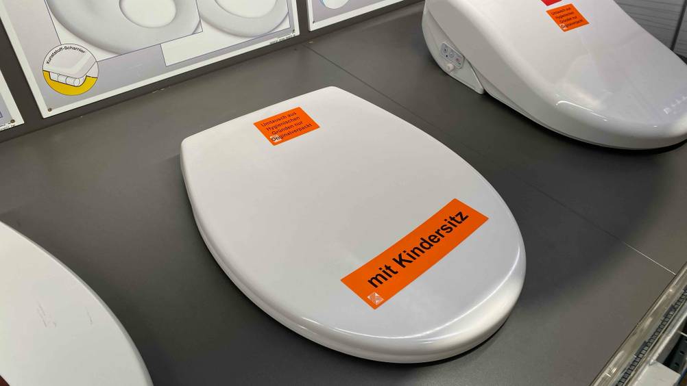 Familien-WC-Sitz getestet: Ein zugeklappter Sitz mit verbautem Kindersitz in einer Ausstellung montiert.