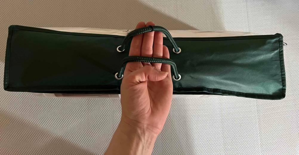 Im Test: Eine Hand greift durch die Trageschlaufen einer verpackten Bettdecke in 155x220 cm von oben.