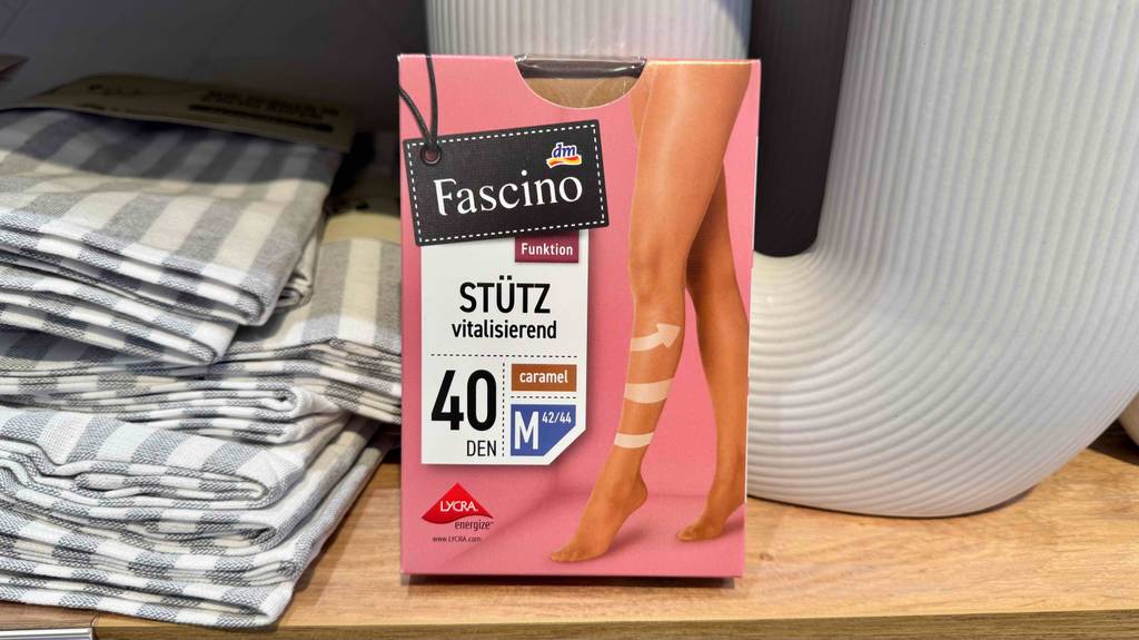 In einem Regal mit Stofftüchern steht eine Packung mit einer Stützstrumpfhose in Größe M und Farbe caramel zum testen.