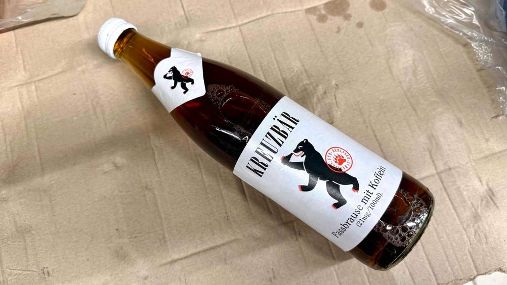 Eine Flasche der getesteten Fassbrause liegt horizontal auf einem Karton.