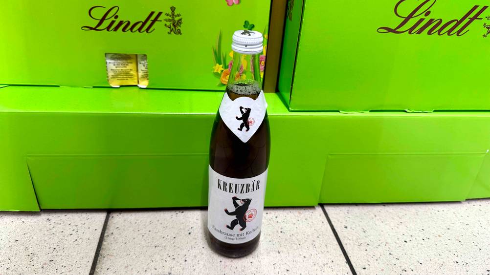 Eine Fassbrause im Test vor mehreren grünen Kartons auf dem Boden.