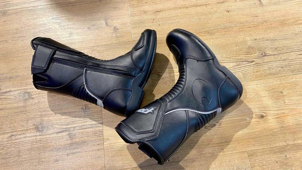 Zwei Motorradstiefel im Test nebeneinander auf der Seite liegend auf einem Holzboden.
