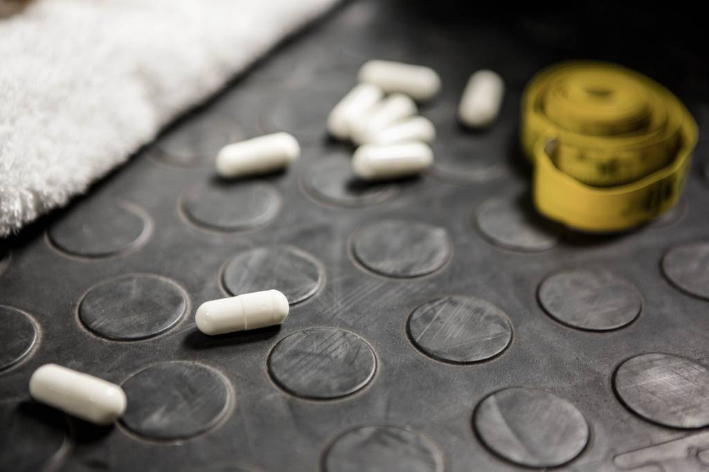 Fatburner-Test: Auf einem Trainingsboden liegen Fatburner-Kapseln und ein Handtuch. 