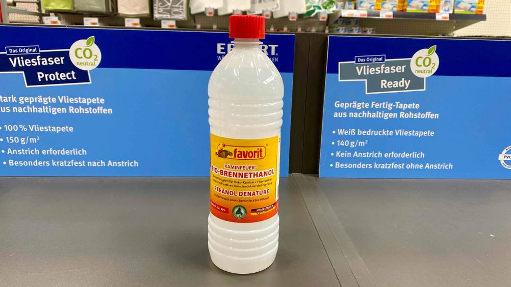 Eine Flasche Bioethanol im Test vor Plakaten in einer Verkaufsfläche.
