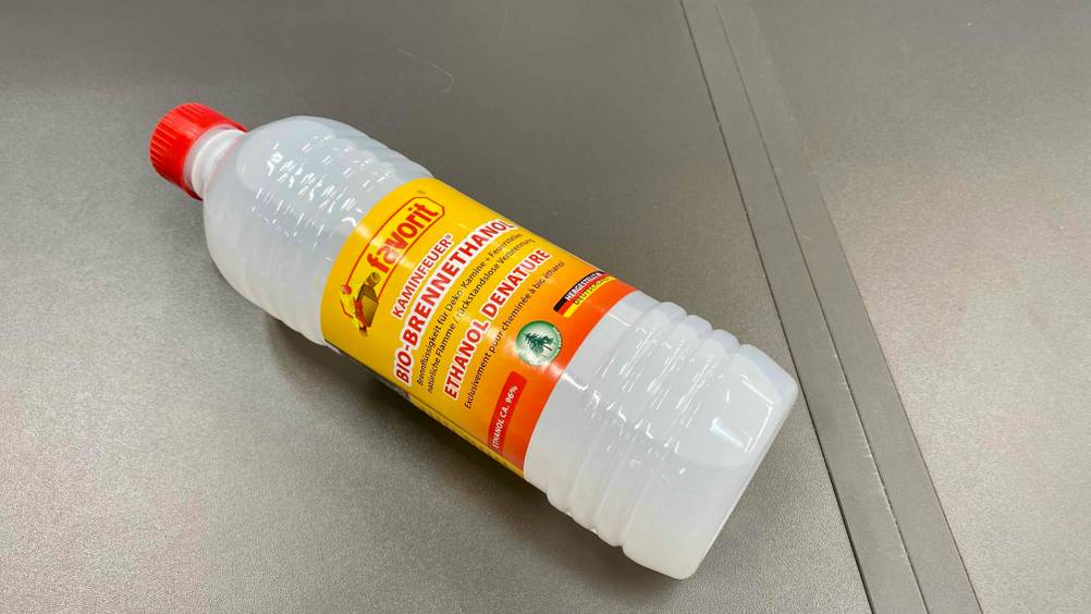 Bioethanol getestet: Eine Flasche liegt quer auf einer Metalloberfläche mit Fokus auf den Boden.