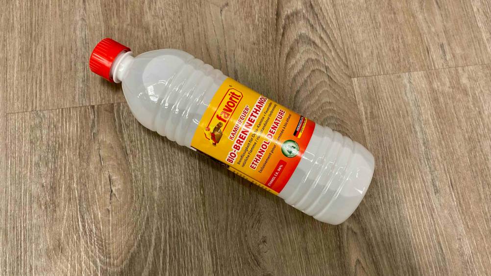 Eine Flasche getesteter Bioethanol liegt quer auf einem Holzboden.