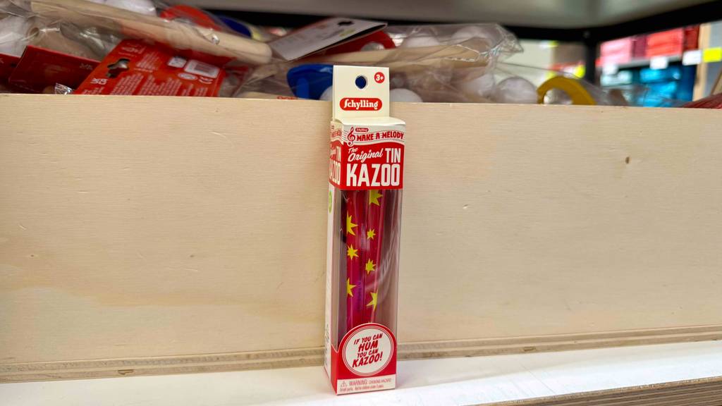 Im Test: Ein Kazoo steht in der transparenten Kartonverpackung vor einer Holzkiste.