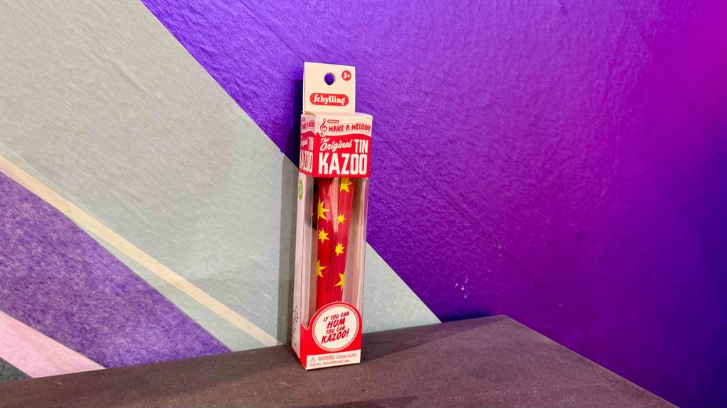 Im Test: Ein Kazoo steht verpackt vor einer lila-weiß-gestreiften Wand.