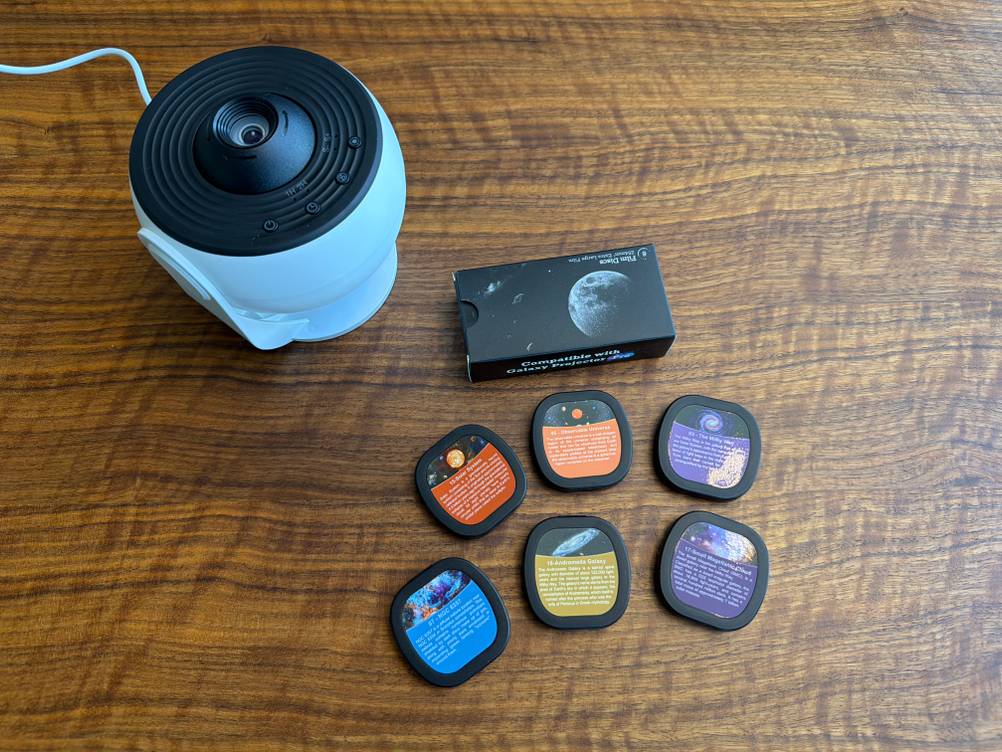 Der Febotak-Aurora-Projektor L03 liegt neben sechs verschiedenen Dias auf einem Tisch.