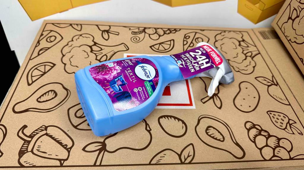 Eine Flasche getesteter Febreze-Textilerfrischer liegt auf einem Karton mit Lebensmittelsymbolen.