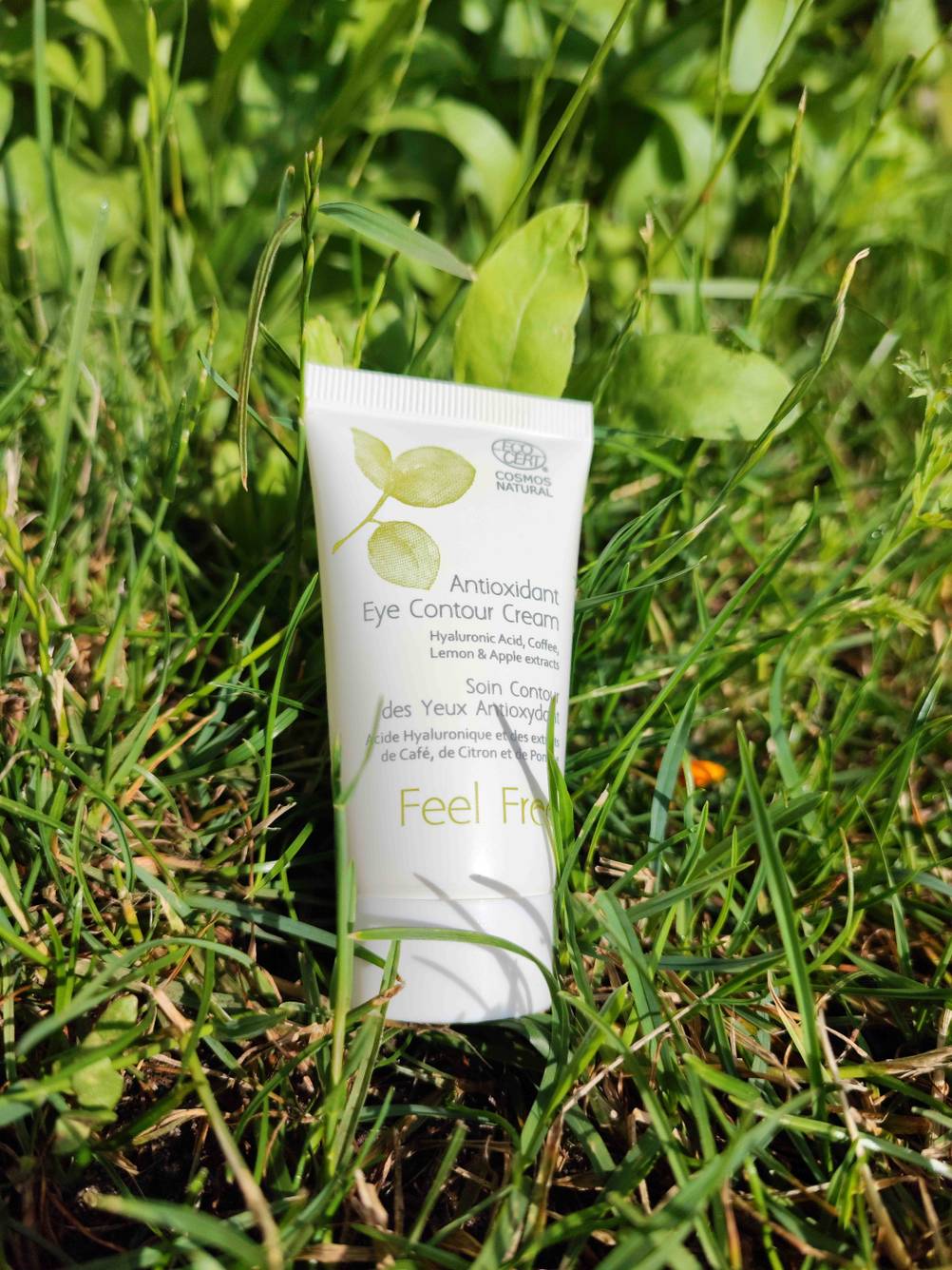 Feel Free Augenkonturcreme in der Tube auf einer Wiese in der Natur.