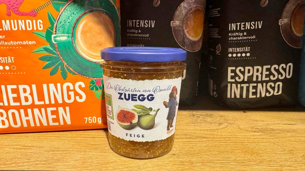Auf einer Holzfläche steht ein Glas Feigenmarmelade im Test vor Kaffeepackungen.