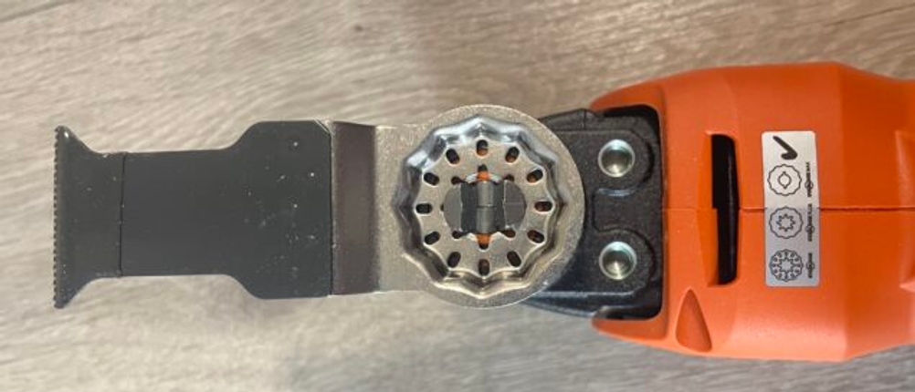Detailaufnahme des Sägeblatts am Fein Multimaster 700 mit Starlock-Aufnahme. Das Werkzeug liegt auf einem Holzboden.