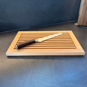 Ein Brotmesser liegt auf dem Feinholz-Brotschneidebrett