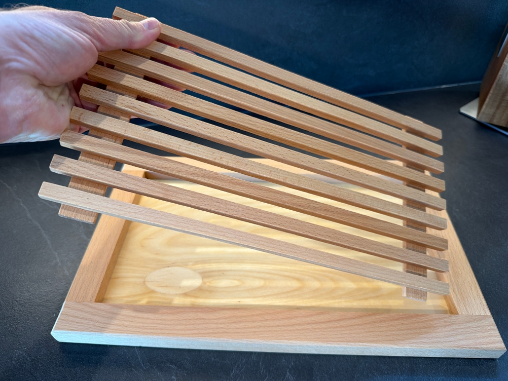 Eine Hand legt den Deckel in das Feinholz-Brotschneidebrett