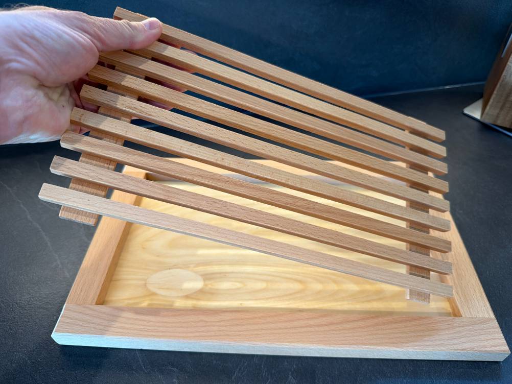 Eine Hand legt den Deckel in das Feinholz-Brotschneidebrett