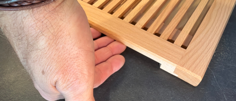 Eine Hand hebt das Feinholz-Brotschneidebrett am Griff hoch