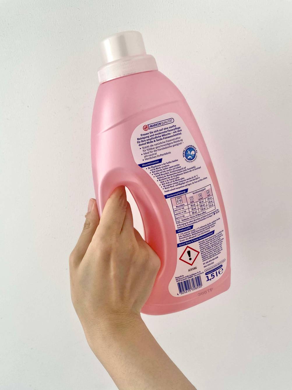 Feinwaschmittel getestet: Eine Hand hält die Rückseite der Flasche vor eine helle Wand.