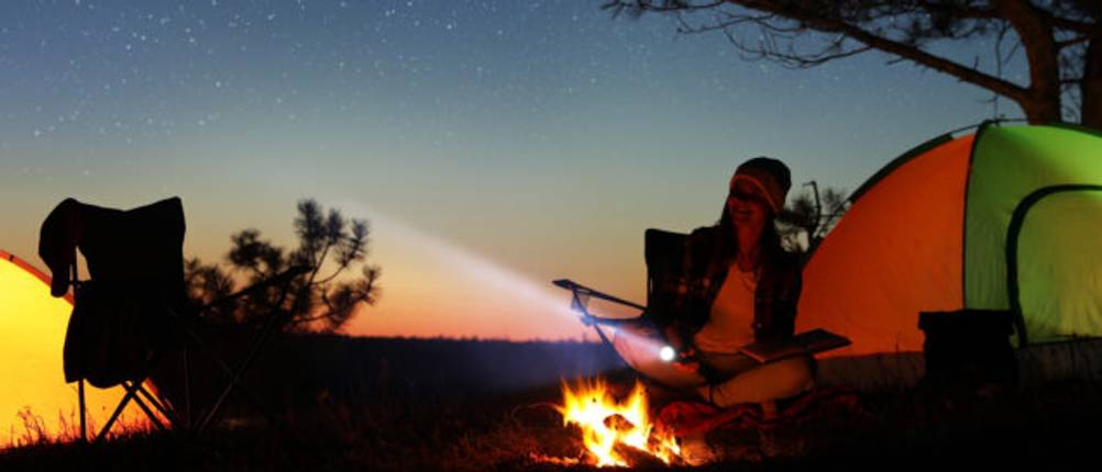Fenix-Taschenlampe-Test: Eine Frau mit einer Taschenlampe bei Nacht vor einem Zelt.