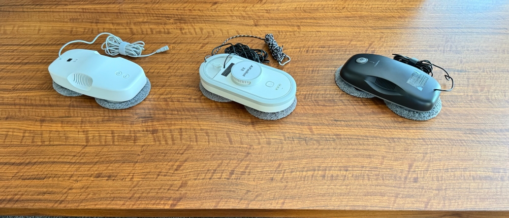 Drei Fensterputzroboter liegen nebeneinander auf einem Tisch