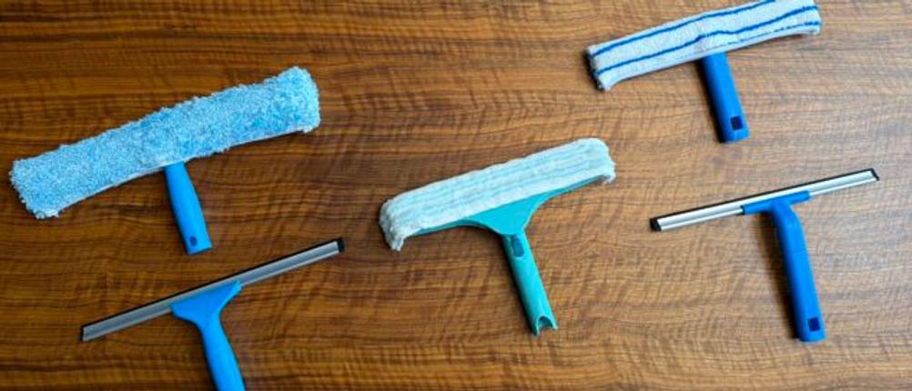 Drei Fensterwischer und zwei Abzieher liegen nebeneinander auf einem Tisch