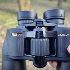 Nahaufnahme des zentralen Fokussierrades des Nikon-Aculon-A211-12x50-Fernglases. Das Nikon-Logo und die Modellbezeichnung sind in Gold aufgedruckt.