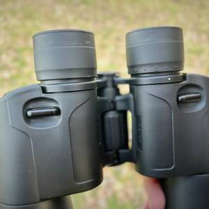 Nahaufnahme der Anbringung des Tragegurts am Olympus-10x50-S-Fernglas. 