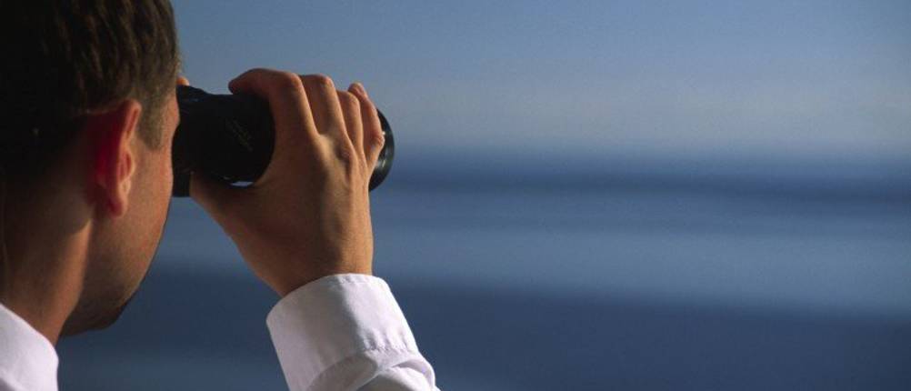 Mann schaut durch ein Fernglas auf den Horizont