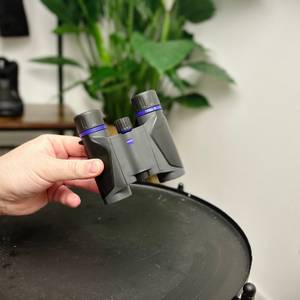 zeiss terra ed pocket Fernglas ohne Schutzhülle von einer Hand über einem schwarzen Tisch gehalten.