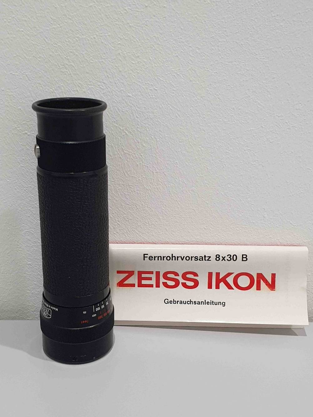 Ein getestetes Fernrohr mit Gebrauchsanleitung vor einer hellen Wand.