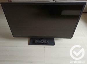 Fernseher auf dem Boden stehend mit Fernbedienung.