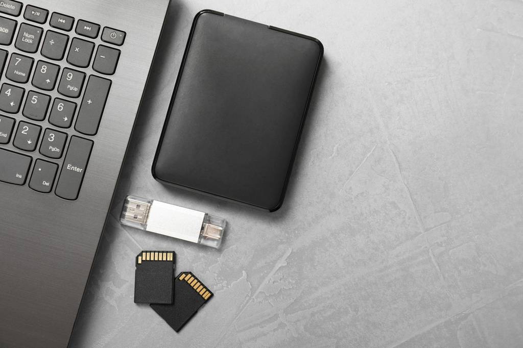 Festplattengehäuse-Test: Eine Festplatte, ein USB-Stick und zwei Speicherkarten liegen neben einem Laptop.