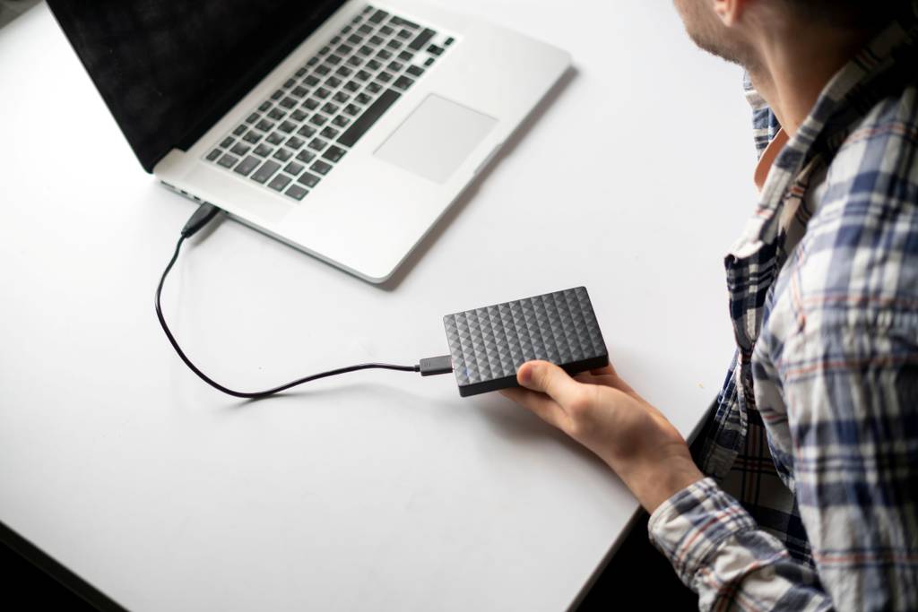 Festplattengehäuse-Test: Ein Mann sitzt vor einem Laptop, an den eine externe Festplatte angeschlossen ist.