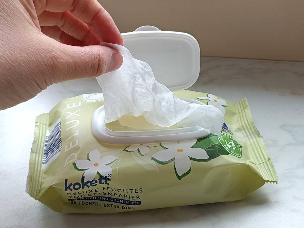 Eine Hand zieht ein Tuch des getesteten feuchten-Toilettenpapiers aus der Packung.