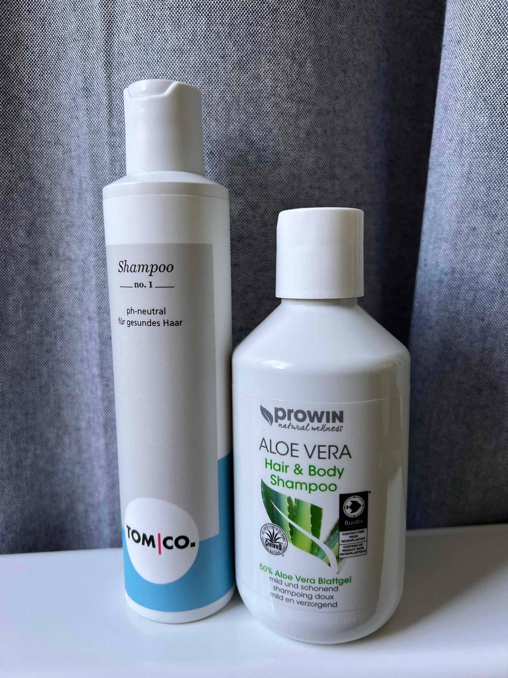 Im Test: Zwei unterschiedliche Flaschen Feuchtigkeitsshampoo nebeneinander vor einem grauen Vohang.