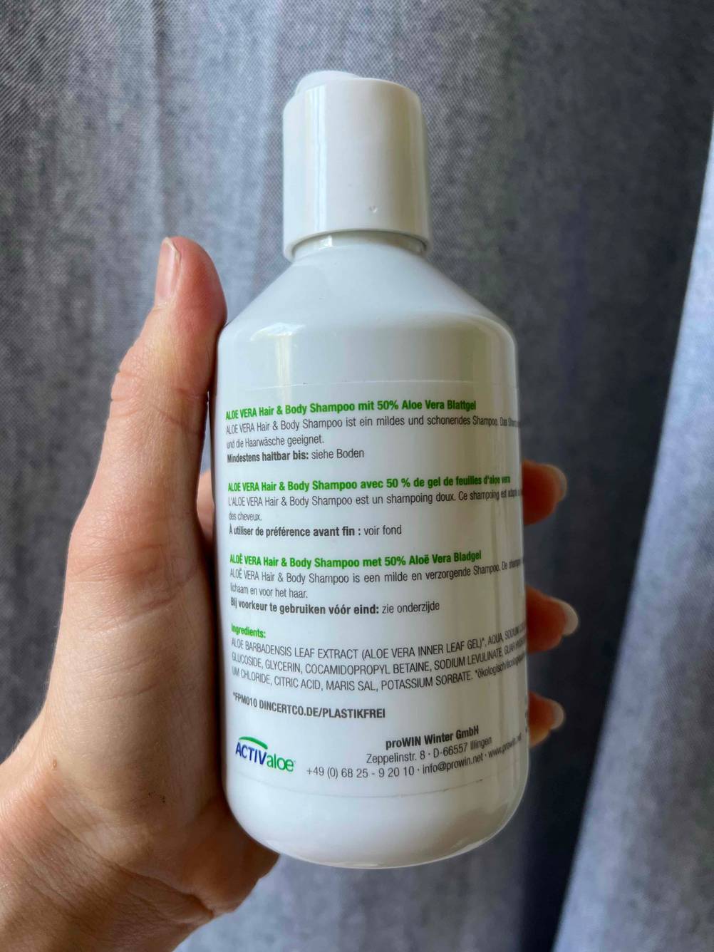 Die Rückseite einer Flasche des getesteten Feuchtigkeitsshampoo von einer Hand vor eine graue Fläche gehalten.