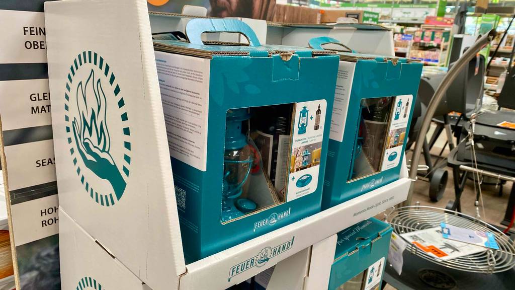 Im Baumarkt stehen auf einem Verkaufsregal mehrere weiß-türkisfarbene Verpackungen mit türkisfarbigen Sturmlaternen im Test.
