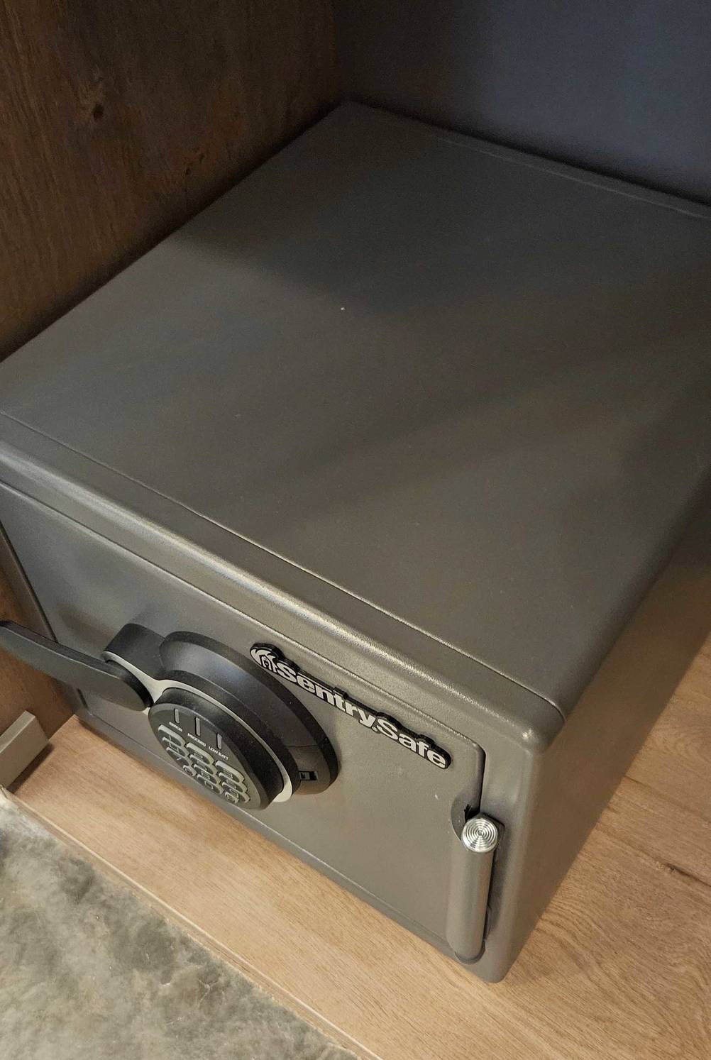 Ansicht von oben auf einen metallfarbenen feuerfesten Tresor im Test der Marke SentrySafe, der sich in einem Holzmöbel befindet.