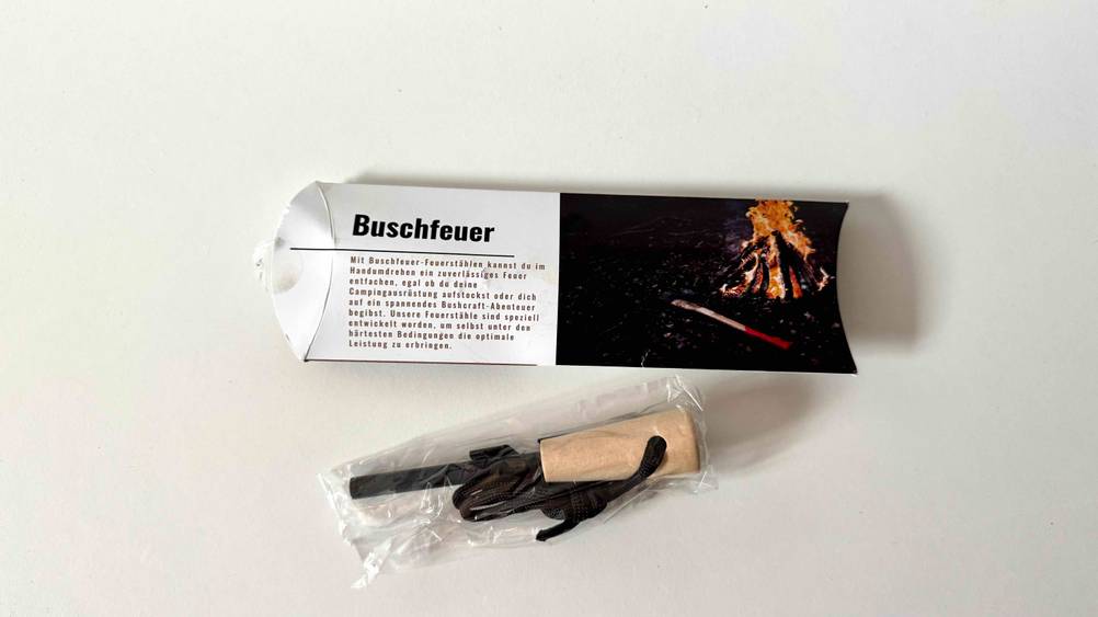 Ein in transparentem Plastik eingepackter Feuerstahl im Test neben seiner Originalverpackung.