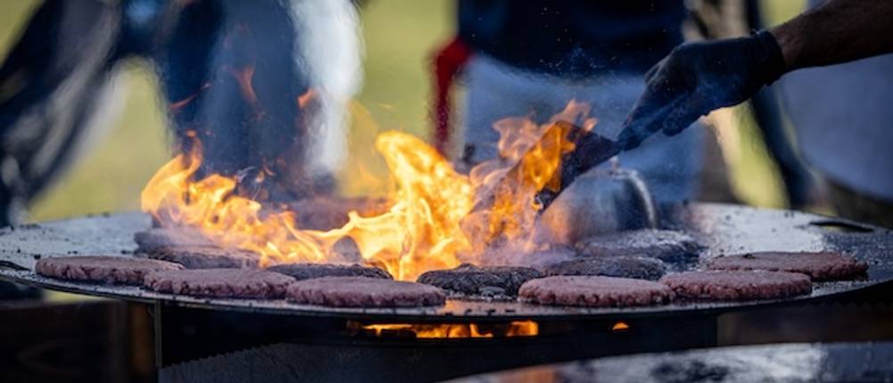 Eine getestete Feuertonne mit Grillrost mit Burgerfleisch in Nahaufnahme.