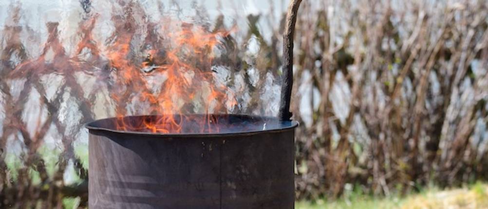 Feuertonne im Test: Eine braune Feuertonne mit loderndem Feuer aus der ein Ast ragt.