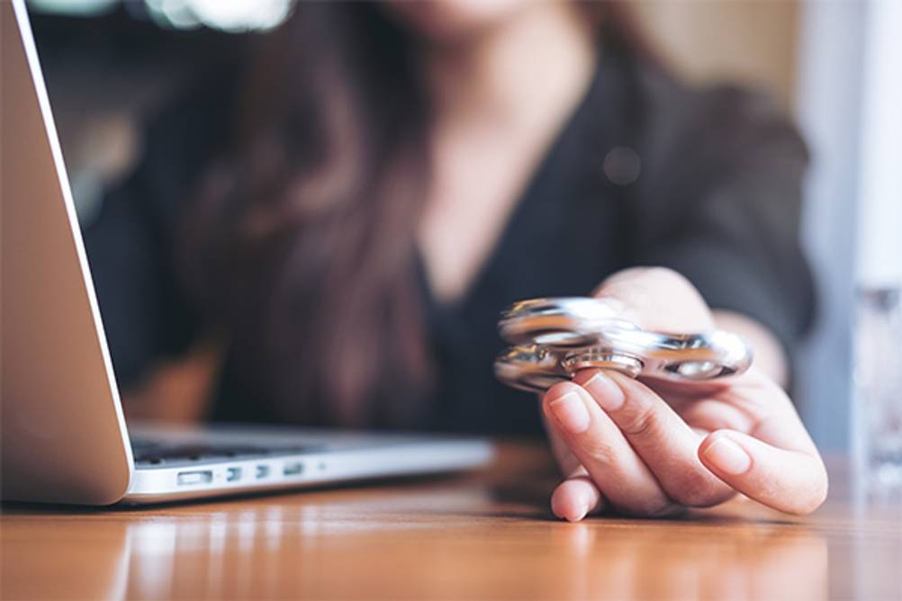 Fidget Spinner im Test: Eine Frau vor einem Laptop mit einem Fidget Spinner in der Hand.