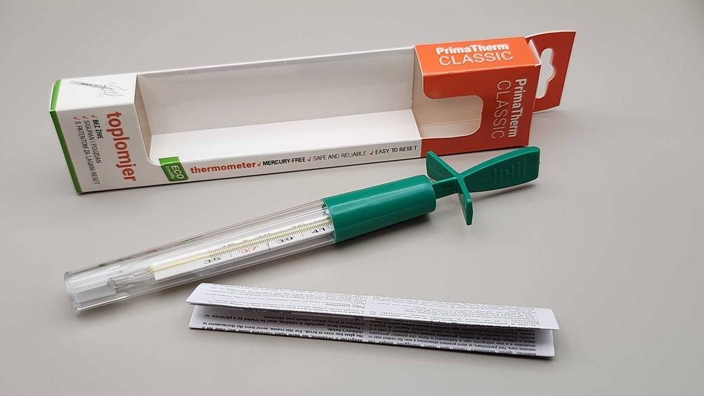 Getestet: Auf einer hellen Fläche liegen die Originalverpackung, das Fieberthermometer analog und der Beipackzettel hintereinander.