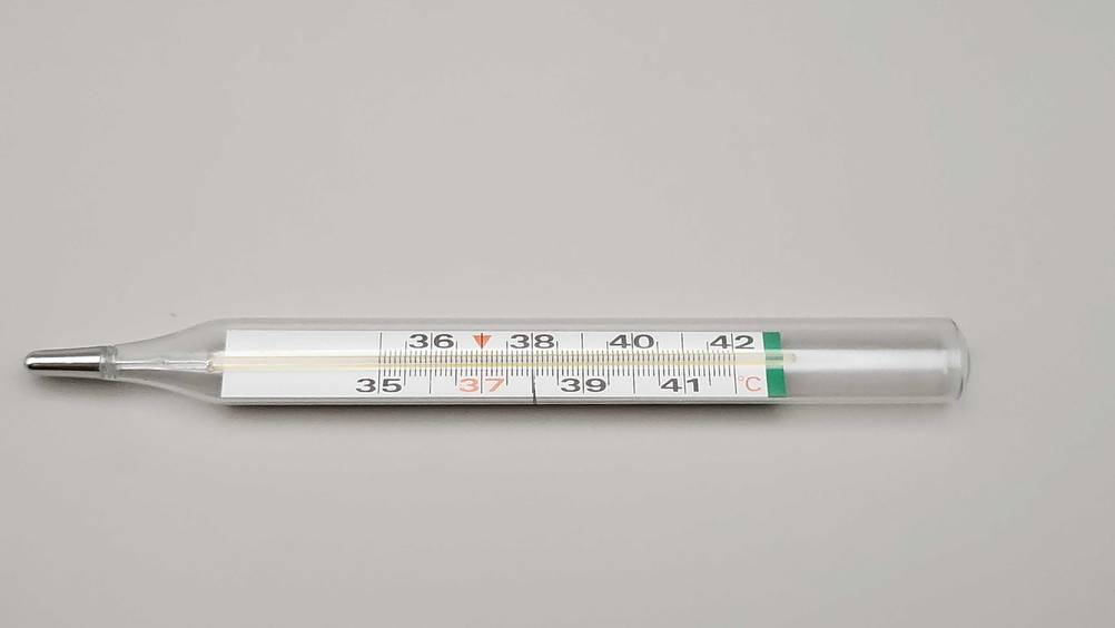 Auf einer hellen Fläche liegt horizontal ein getestetes Fieberthermometer analog.
