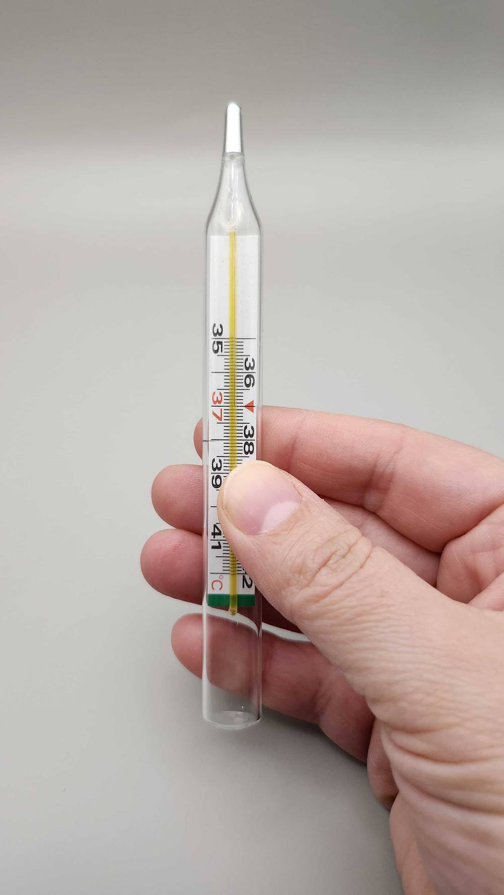 Eine Hand hält ein Fieberthermometer analog im Test.