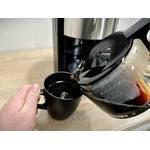 Kaffee wird aus der Glaskanne der Krups KM3210 in eine schwarze Tasse gegossen. Die Tasse wird mit einer Hand gehalten.