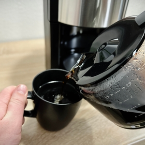 Kaffee wird aus der Glaskanne der Krups KM3210 in eine schwarze Tasse gegossen. Die Tasse wird mit einer Hand gehalten.