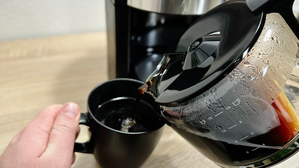 Kaffee wird aus der Glaskanne der Krups KM3210 in eine schwarze Tasse gegossen. Die Tasse wird mit einer Hand gehalten.