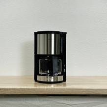 Die Krups KM3210 Pro Aroma Plus Filterkaffeemaschine steht auf einer Holzarbeitsplatte. Daneben befinden sich eine schwarze Tasse und ein Kaffeelot.