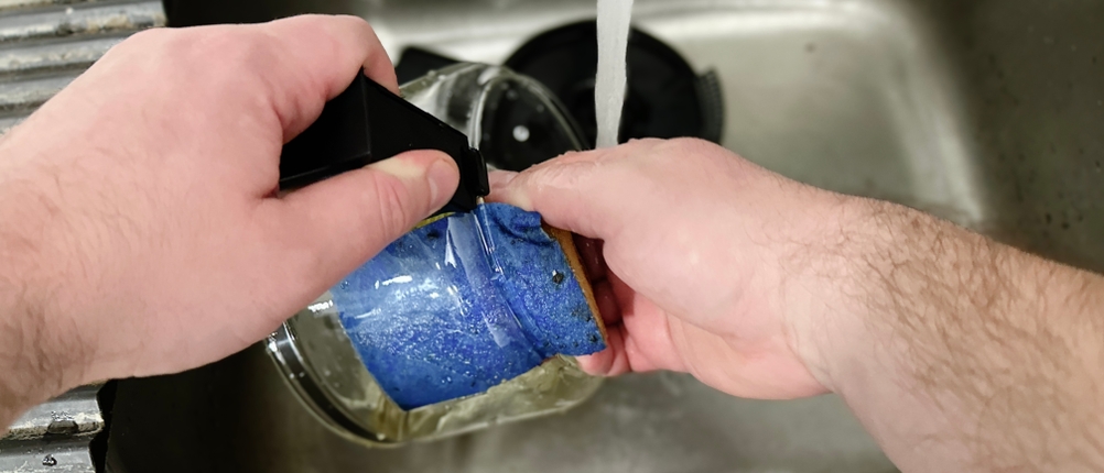 Eine Glaskanne der Krups KM3210 wird unter fließendem Wasser gereinigt. Die Hand hält die Kanne mit einem Schwamm.